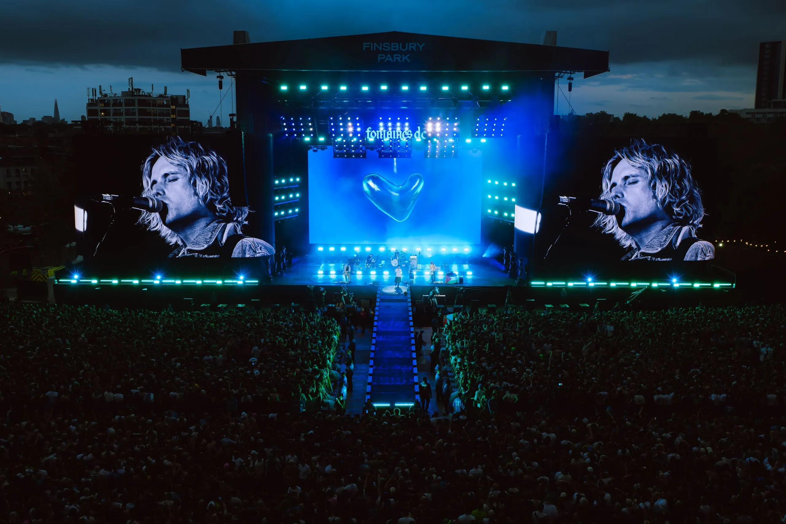 Finsbury Park stage at blue hour, with black-and-white close-ups of the singer on the side screens and a chrome heart on the centre screen.