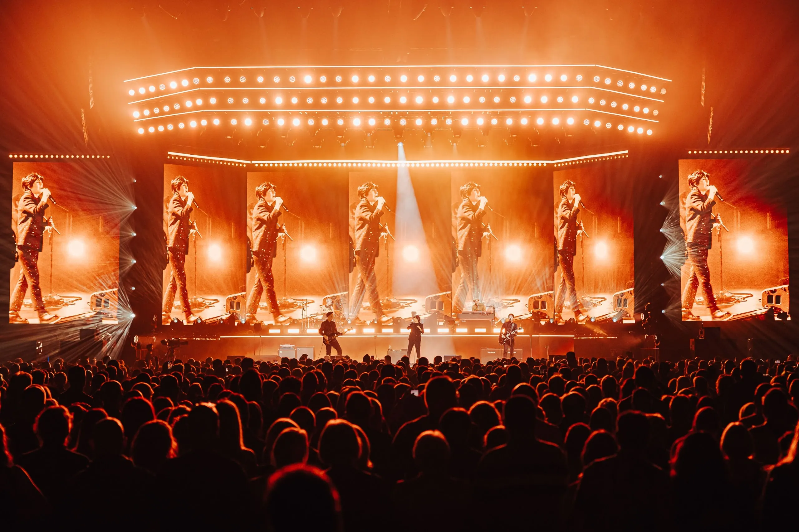 Seven portrait screens repeating footage of the singer in warm orange light, with the band on stage below