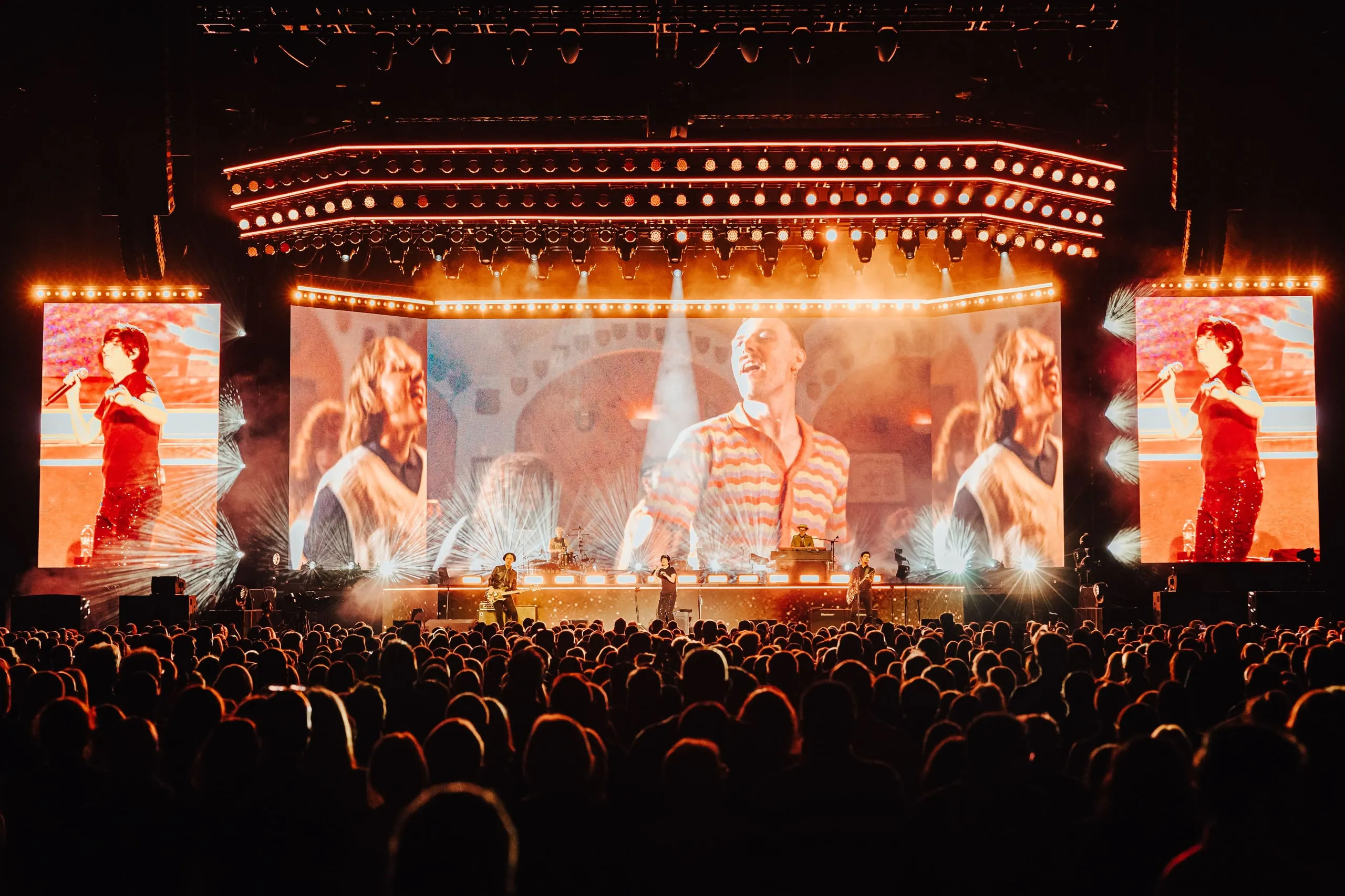 Close-up footage of band members across the main LED wall and side screens, with bursts of light framing the stage