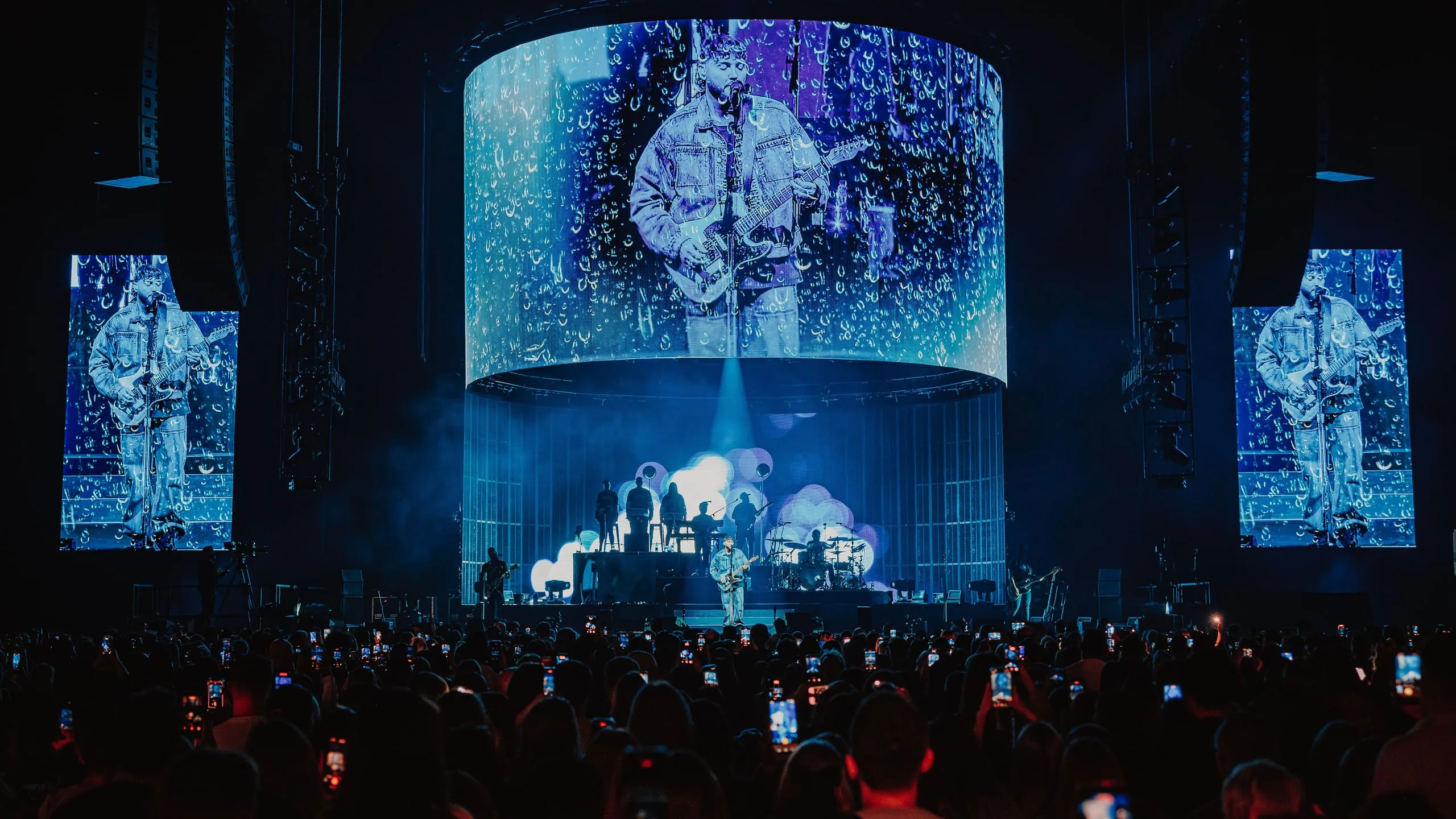 James Arthur on guitar shown on the cylinder screen under a falling-raindrop effect, mirrored on the side screens