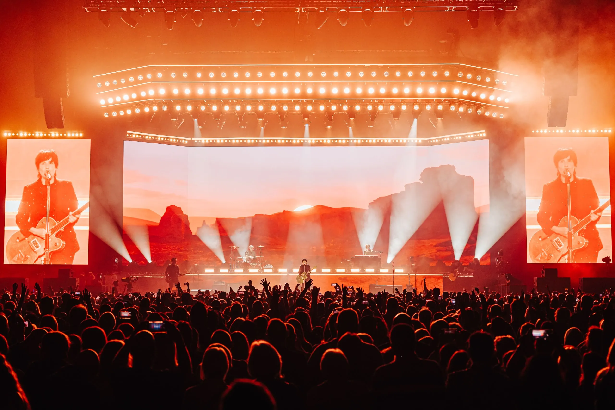 Desert sunset landscape on the main screen cut by beams of light, with close-ups of the singer playing guitar on the side screens