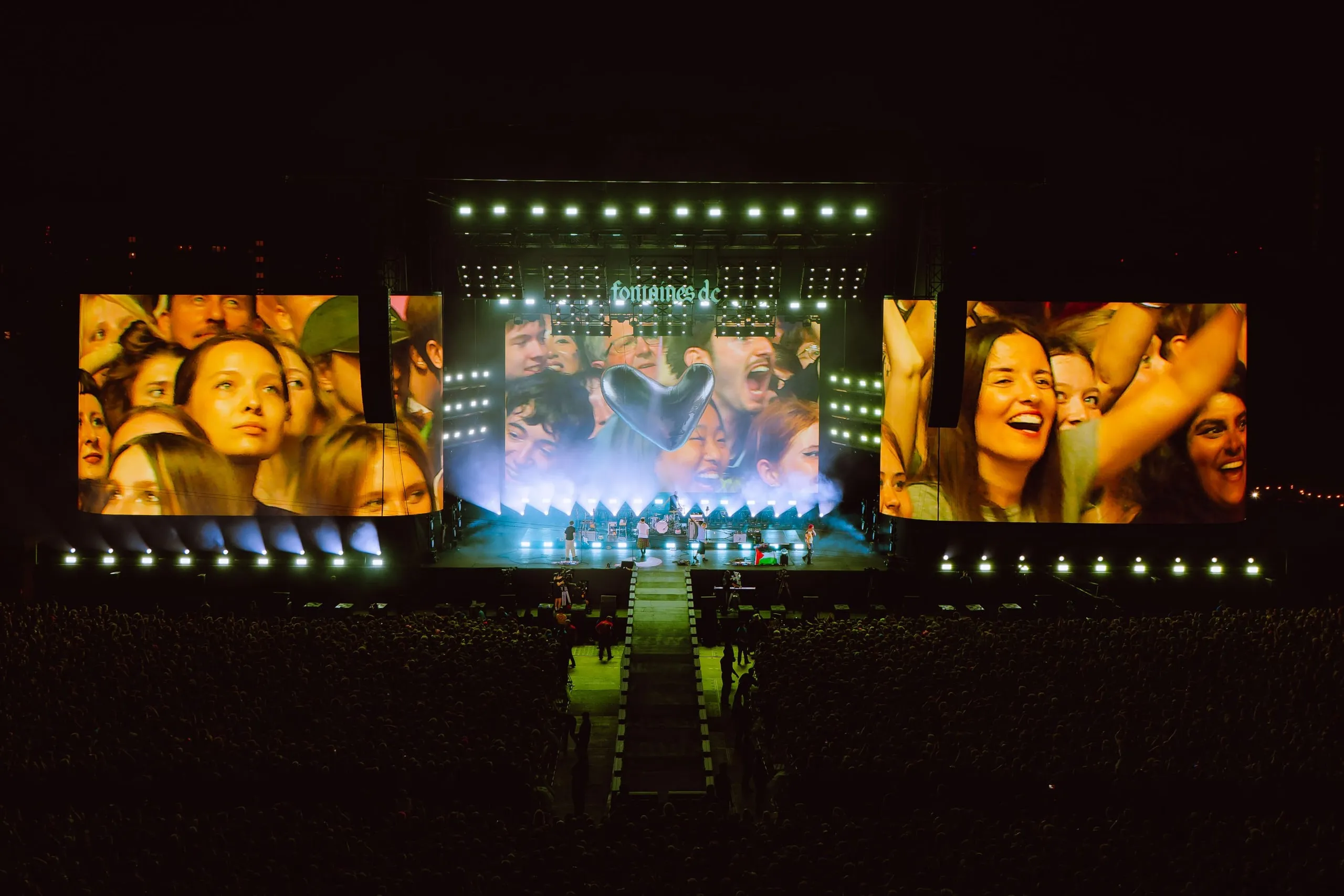 Crowd-camera shots of singing fans on all three screens at Finsbury Park, with a heart graphic at the centre